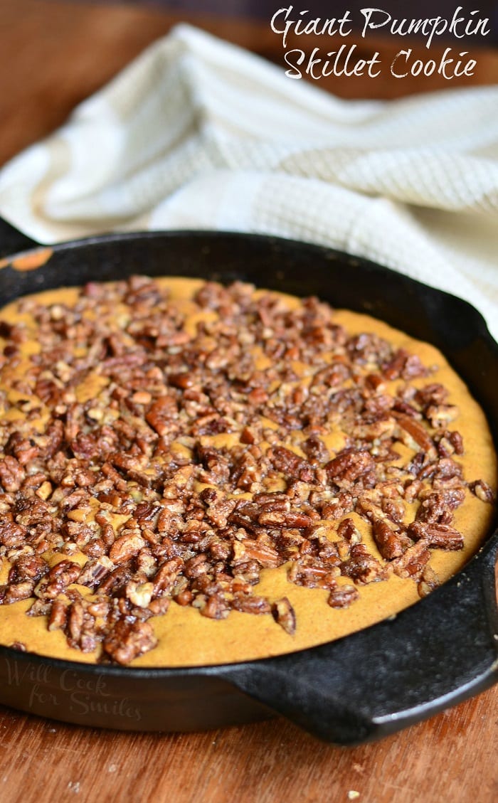 black skillet with a giant pumpkin cookie while sitting on a wooden table with a white cloth in the background