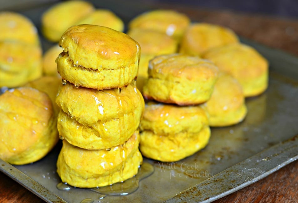 Honey Pumpkin Biscuits stacked up together with honey over them on a cookie sheet