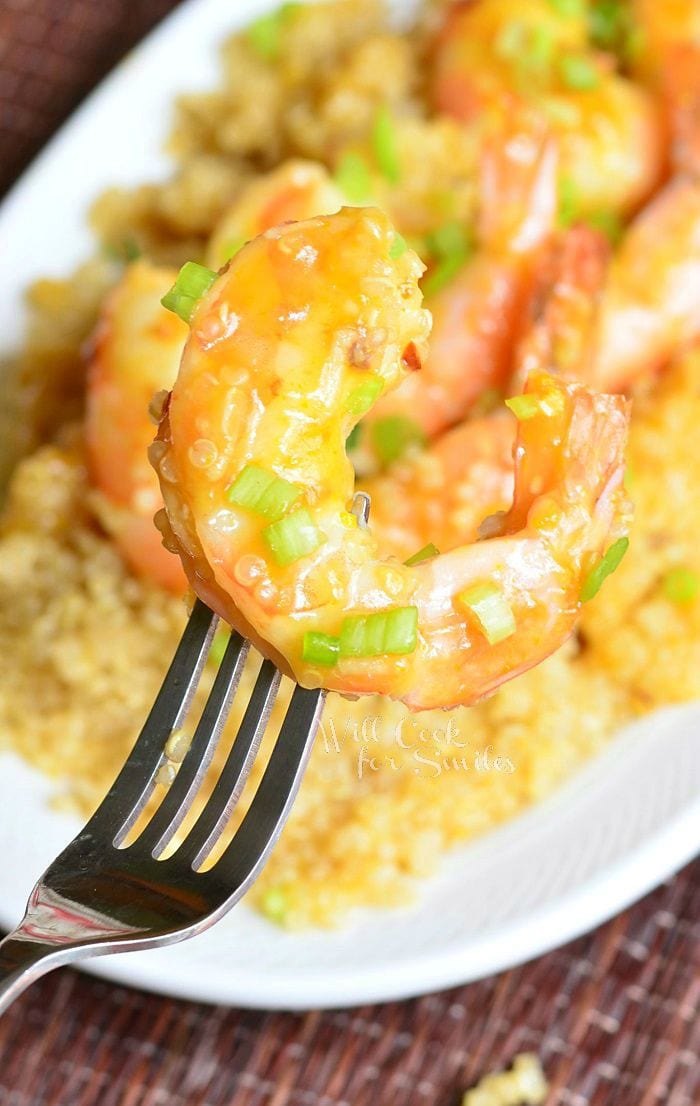 Orange Shrimp on a fork with Quinoa in the background on a white plate 