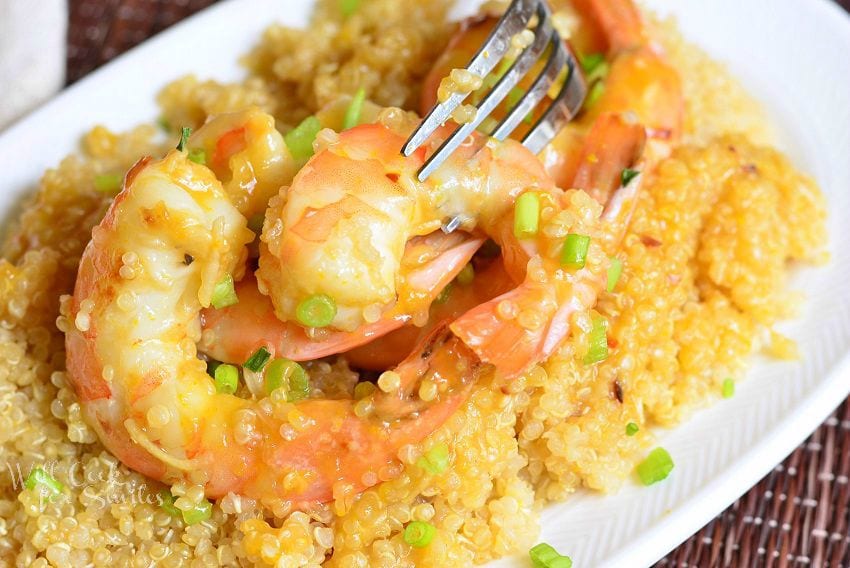 Orange Shrimp with Quinoa in a white bowl with a fork in one of the shrimp