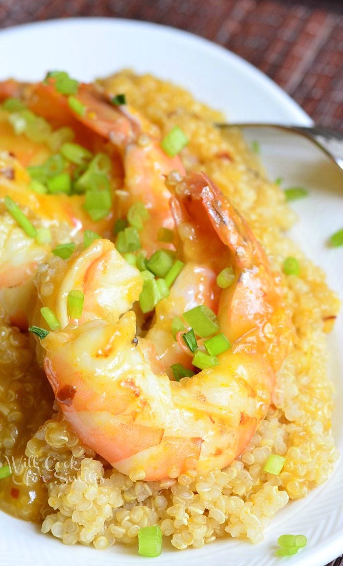 Oval white plate with light orange shrimp with quinoa with a fork resting at the right of the dish