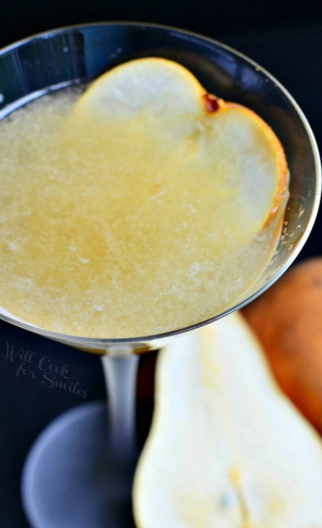 Top view of the Pear Martini in a tall martini glass. The liquid is yellow-ish in color. A thinly sliced piece of pear is on the inside of the glass for garnish.