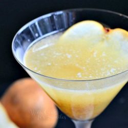 A martini glass filled with pear martini with a halved pear resting at the base of the glass