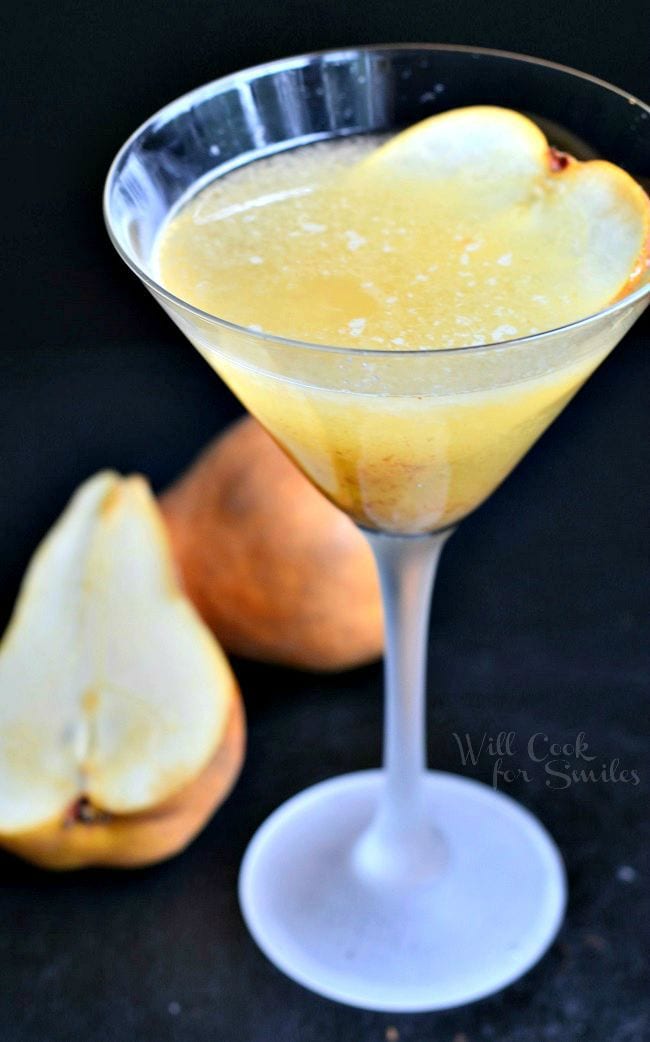The Pear Martini is in a tall martini glass. The liquid is yellow-ish in color. Pulp has collected towards the bottom of the glass. A thinly sliced piece of pear is on the inside of the glass for garnish.