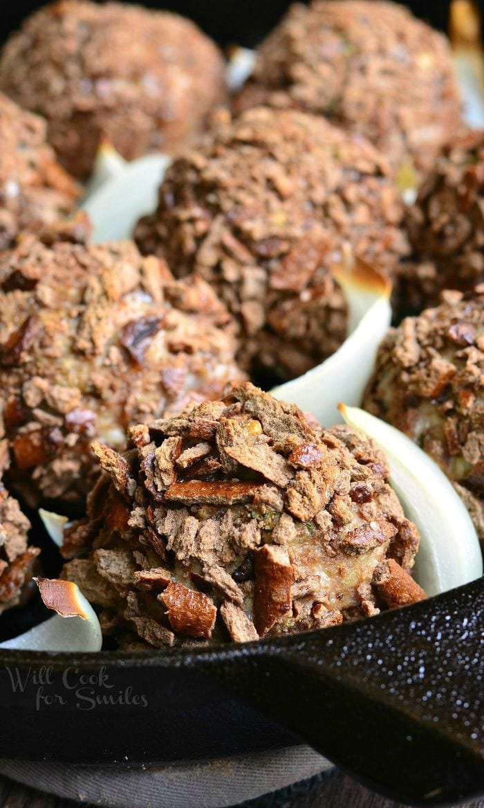 Pretzel Crusted Parmesan Turkey Meatballs and slices of onion in a black skillet.