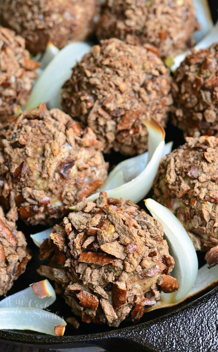 Pretzel Crusted Parmesan Turkey Meatballs and slices of onion in a black skillet.