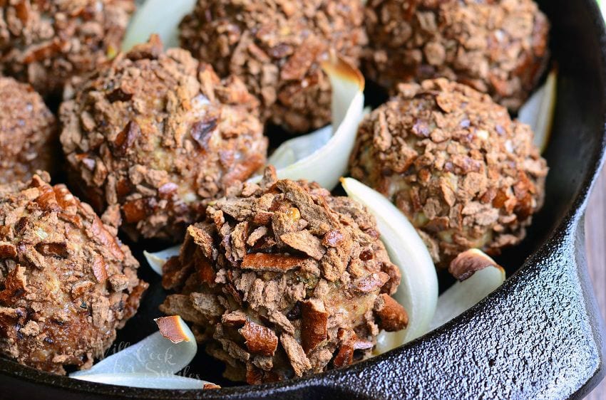 Pretzel Crusted Parmesan Turkey Meatballs and slices of onion in a black skillet.