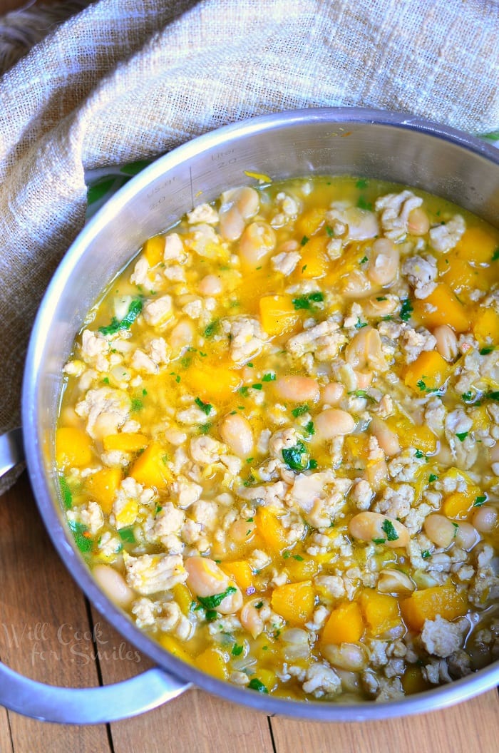 Pumpkin Chicken Chili with pieces of pumpkin, ground chicken, and white beans in a metal pot 