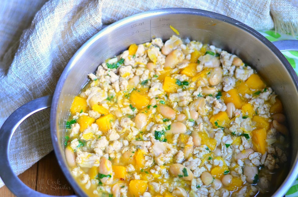 Pumpkin Chicken Chili with pieces of pumpkin, ground chicken, and white beans in a metal pot 