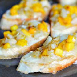 Pumpkin pear brie crostinis on a black surface viewed close up