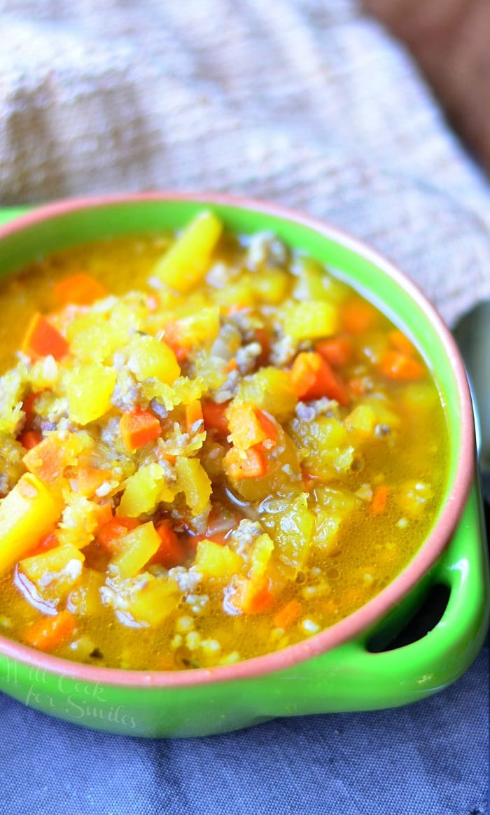 green clay bowl filled with pumpkin sausage soup resting on several cloths
