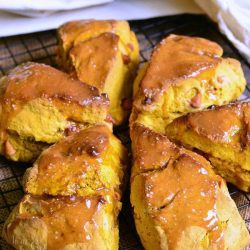 6 salted caramel butterscotch pumpkin scones on a wire colling rack over a tan cloth with a white and blue striped cloth in the background