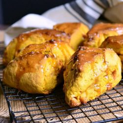 6 salted caramel butterscotch pumpkin scones on a wire colling rack over a tan cloth with a white and blue striped cloth in the background