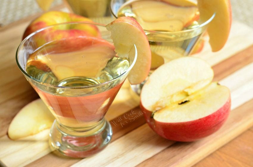 {Skinny} Cinnamon Apple Champagne Martinis in short martini glasses with a sliced apple placed on the rim of each glass. On the table there are also apples and apple slices.