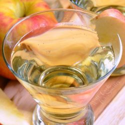 3 martini glasses filled wth skinny cinnamon apple champagne martinis on a wooden cutting board with sweet N low packets and apples spread around the glasses viewed from close up and above