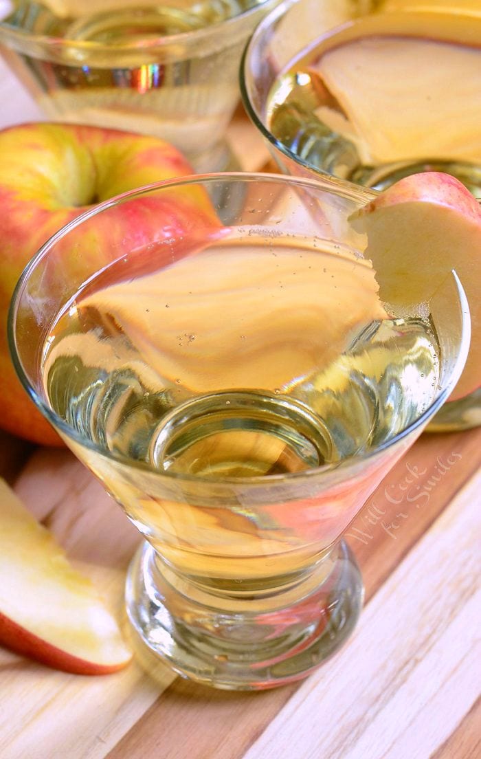3 martini glasses filled wth skinny cinnamon apple champagne martinis on a wooden cutting board with sweet N low packets and apples spread around the glasses viewed from close up and above