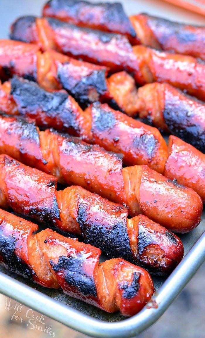 Spiral cut Hot Dogs lay side by side in a pan. They appear juicy and have black grill marks on them.