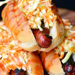 3 buns filled with sriracha honey hot dogs and slaw mix on a wooden table hot dogs are stacked in a pyramid