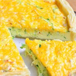 close up view of 1 slice seperated from sriracha zucchini and cheese quiche on a wood table as shown from above