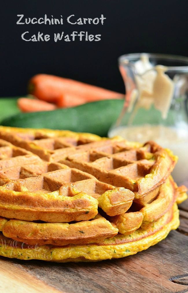 Side view of three Zucchini Carrot Cake Waffles all stacked on top of each other. In the background is a glass container which holds the cinnamon cream cheese sauce.