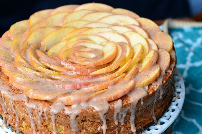 horizonal photo of Cinnamon Glazed Apple Cake with thinly sliced apples on top and a cinnamon glaze on a white cake stand 
