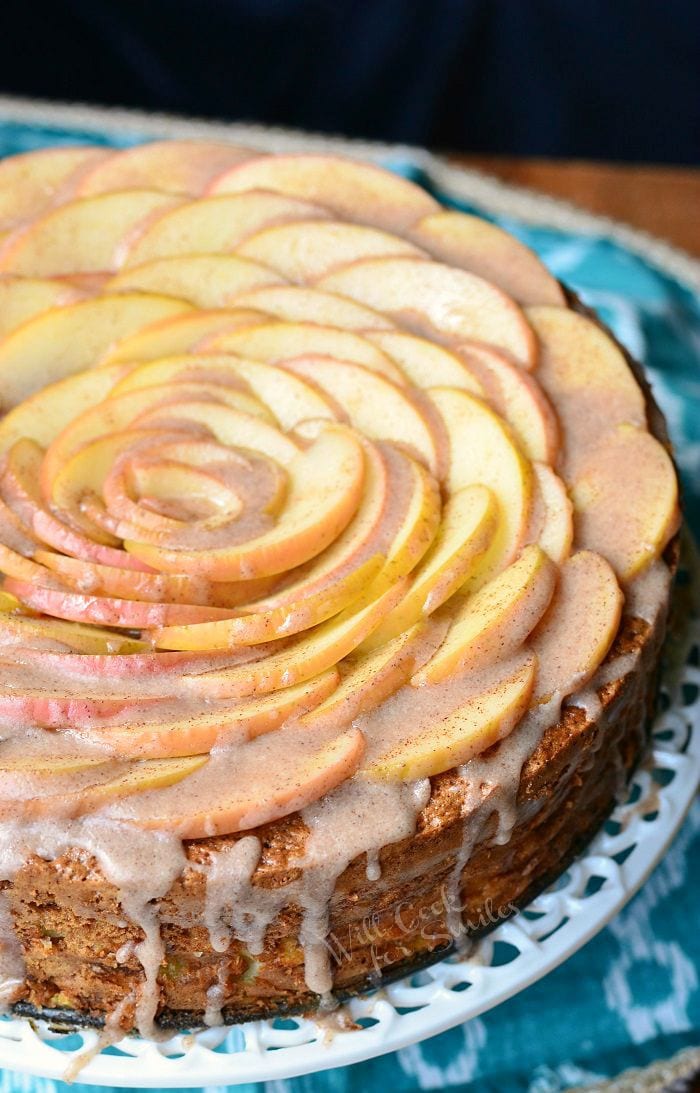 top view photo of Cinnamon Glazed Apple Cake with thinly sliced apples on top and a cinnamon glaze on a white cake stand 