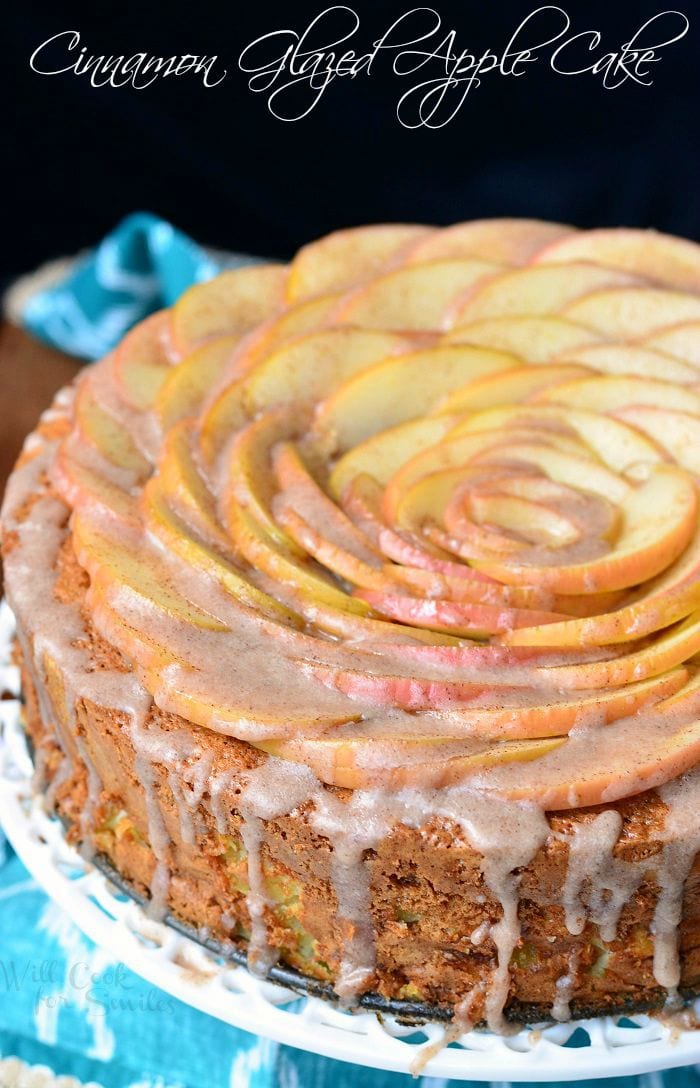 Cinnamon Glazed Apple Cake with thinly sliced apples on top and a cinnamon glaze on a white cake stand 