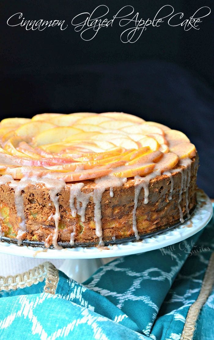 Cinnamon Glazed Apple Cake with thinly sliced apples on top and a cinnamon glaze on a white cake stand 