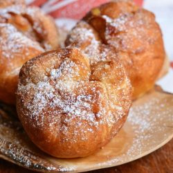 3 easy apple pie doughnuts on a decorative wooden plate with a white and red fall festive cloth in the background