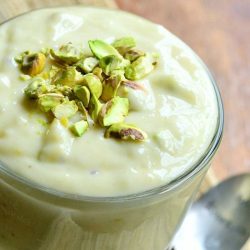 glass dessert dish filled with homemade pistachio puddin on a wooden table with a spoon at the base of the glass viewed close up and above