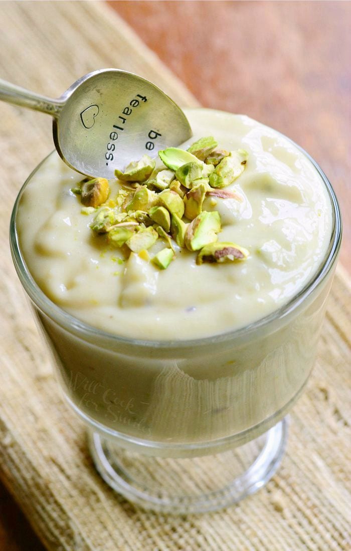 top view of Pistachio Pudding with chopped up pistachios on top in a clear glass bowl with a spoon 