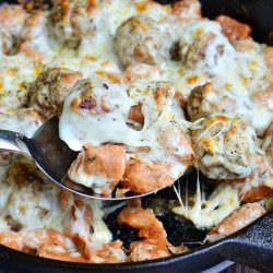 black skillet with meatball and gnocchi bake with a spoon holding up one porion as viewed from above