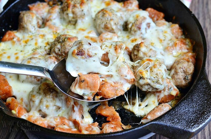 Meatball and Gnocchi Bake being scooped out with a metal serving spoon with cheese on top on a cast iron skillet 