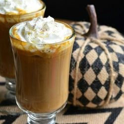 Dessert coffee glass mug filled with pumpkin white chocolate mocha latte on a white and black zig zag placemat with an additional glass in the background to the left next to a fabric pumpkin decoration