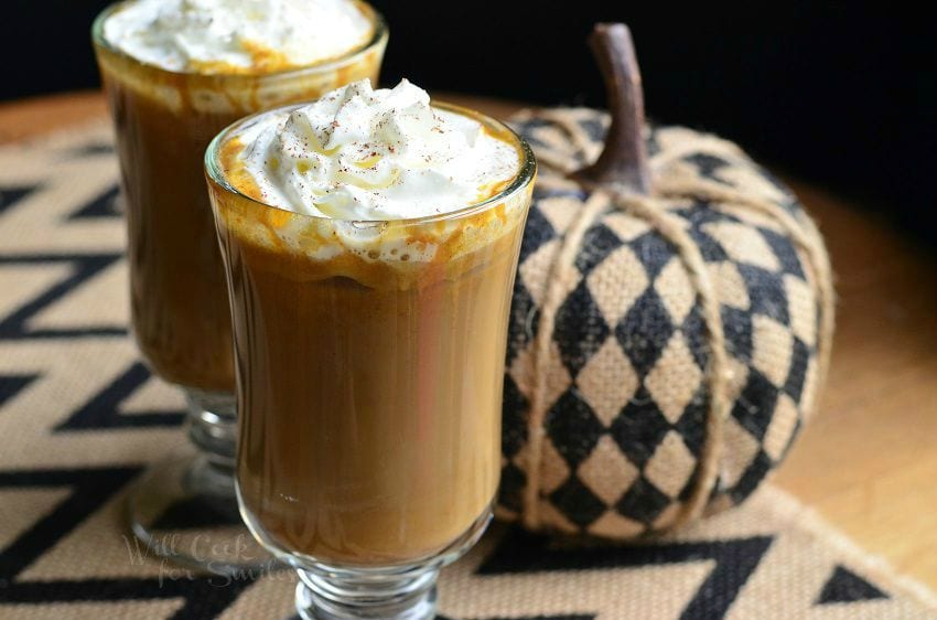 Pumpkin White Chocolate Mocha Latte in a clear glass cut with whip cream on top with a checkered pumpkin to the right 