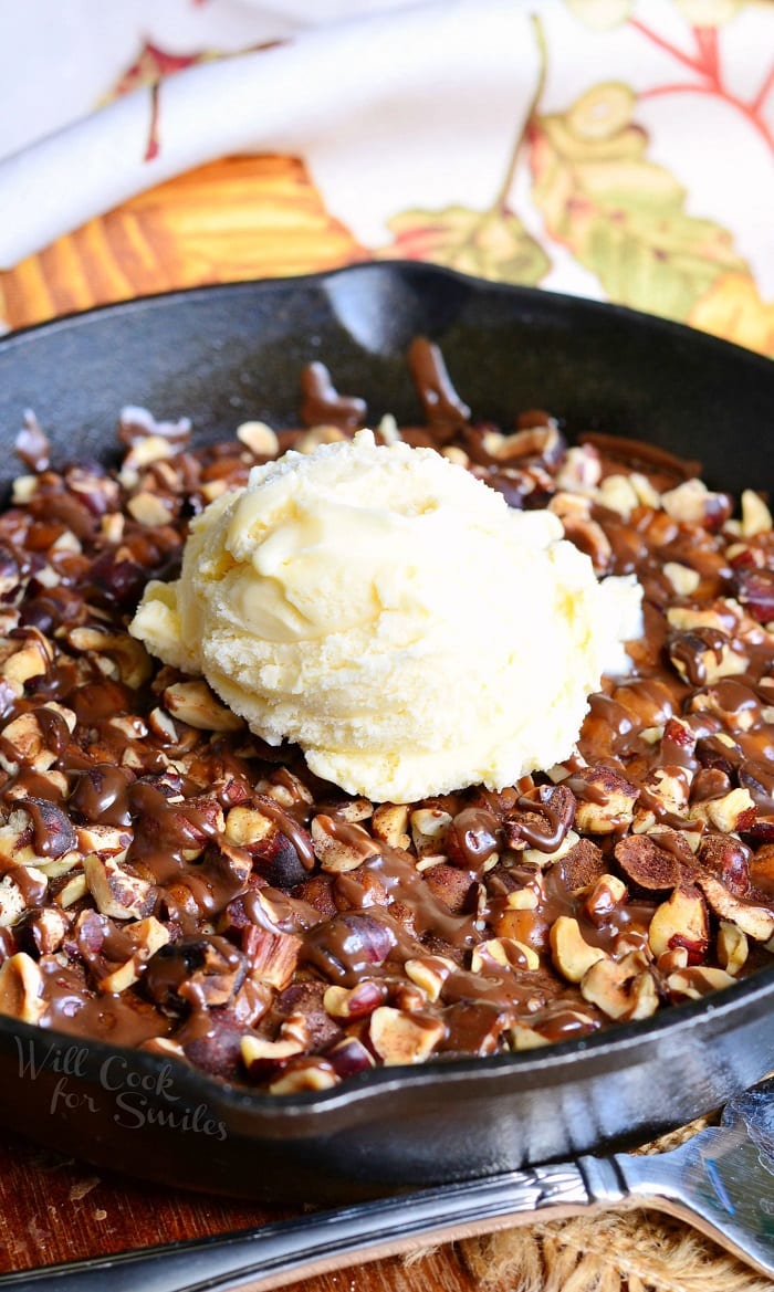 Pumpkin Turtle Brownie Skillet in a cast iron pan with nuts and caramel on top with a scoop of vanilla ice cream in the middle 