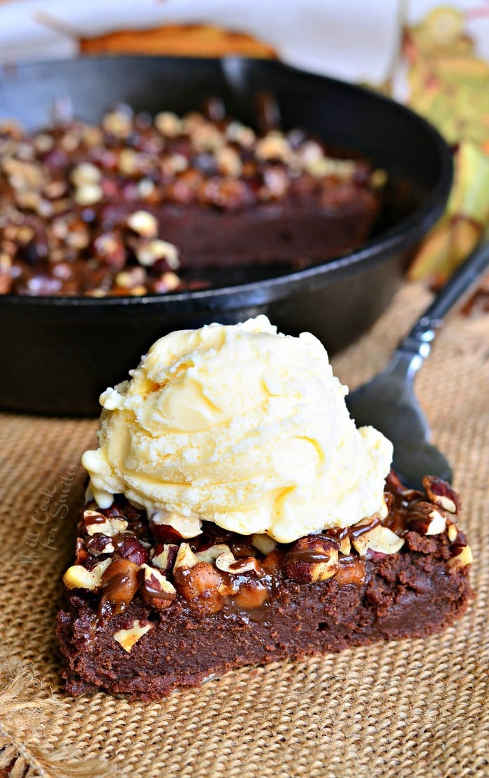 Pumpkin Turtle Brownie slice on a table with vanilla ice cream on top and the rest of the brownie in a cast iron pan 