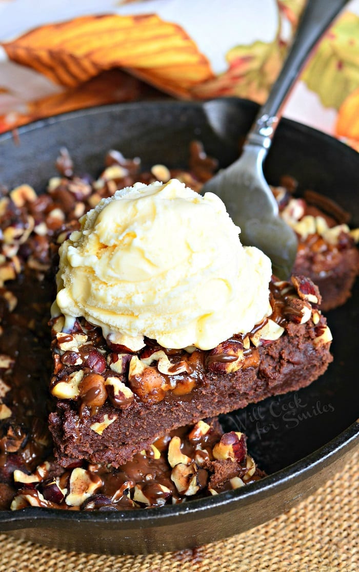 Pumpkin Turtle Brownie slice being lifted out of the cast iron skillet with a pie spatula vanilla ice cream on top and the rest of the brownie in a cast iron pan 