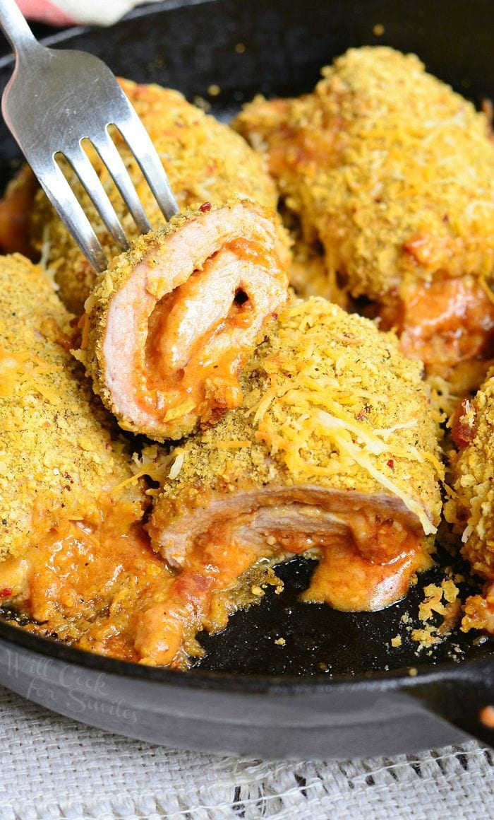black skillet with southwest pork rollups on a white cloth with a white and red cloth in the background with 1 roll cut in half in foreground