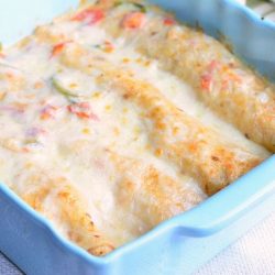 blue baking dish filled with spicy creamy shrimp enchiladas on a white cloth