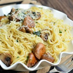 decorative white bowl with truffle pasta and mushrooms on a tan and black placemat on a wooden table as viewed close up