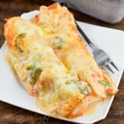 two cheesy shrimp enchiladas on a white plate with a fork next to them.