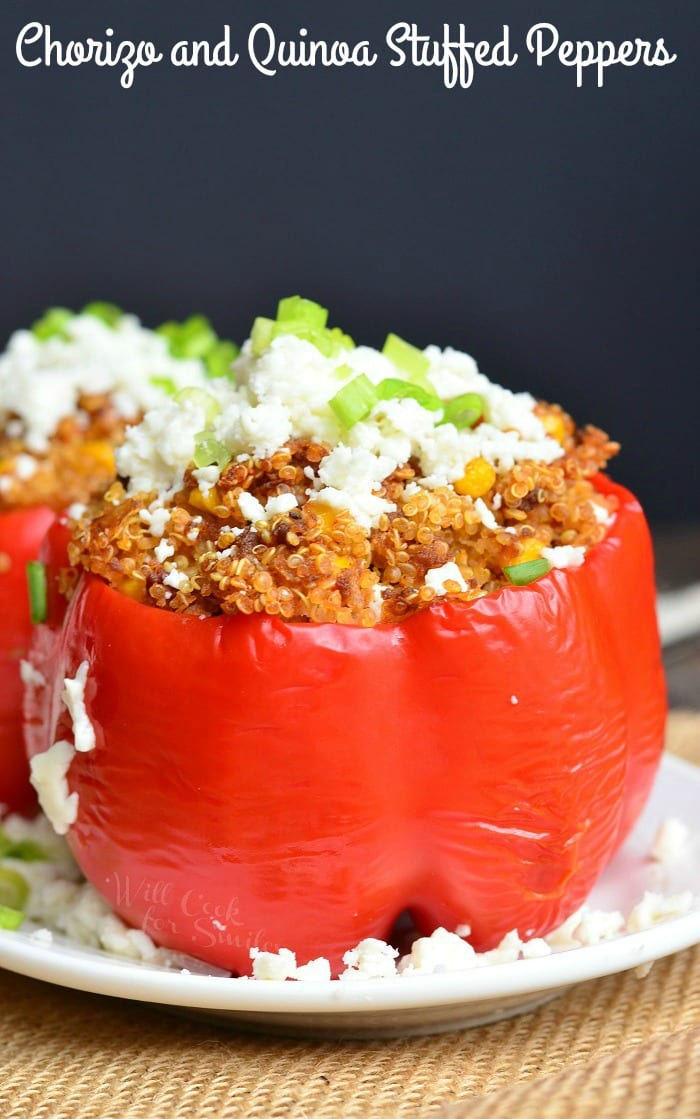 Chorizo and Quinoa red Stuffed Peppers with cheese and green onions on top on a white plate 