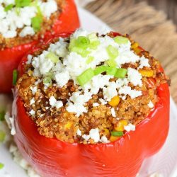 2 chorizo and quinoa stuffed peppers on a white oval plate sitting on a brown placemat on a wooden table as seen from above