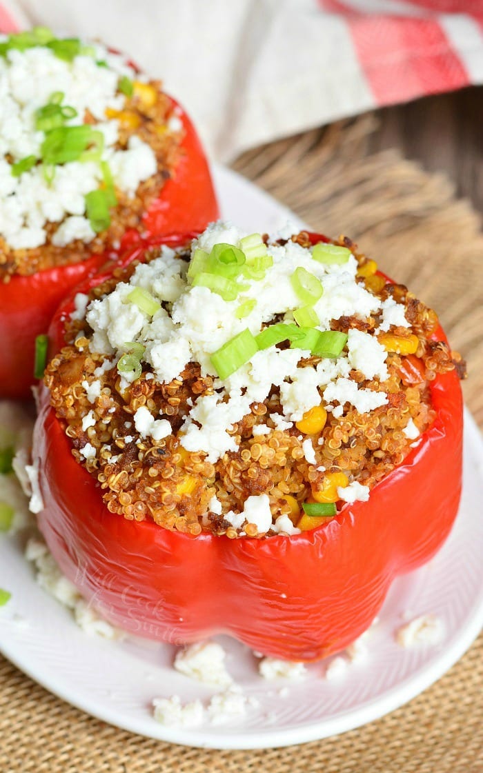 2 chorizo and quinoa stuffed peppers on a white oval plate sitting on a brown placemat on a wooden table as seen from above
