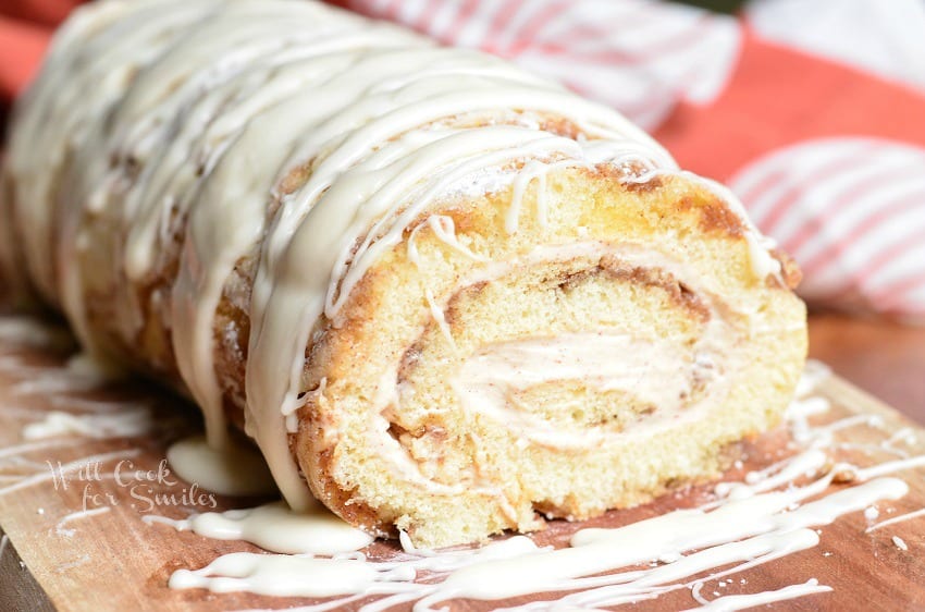 Cinnamon Roll Cake Roll with icing all over the top on a cutting board