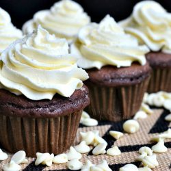 Double chocolate cupcakes with white chocolate cream cheese frosting on a white and black placemat with white chocolate chips scattered around the bottom of the cupcakes as seen close up