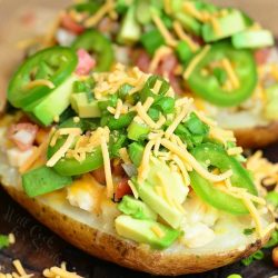 Close up view of fiesta chicken twice baked potatoes on a wooden board topped with chives and sliced jalapenos