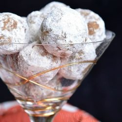 Decorative martini glass filled with pumpkin spice rum balls with a red and white cloth in the background