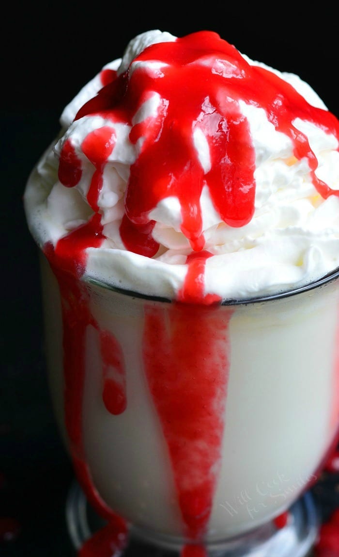 White Chocolate Raspberry Hot Chocolate in a clear glass bowl with whip cream and raspberry sauce on top 